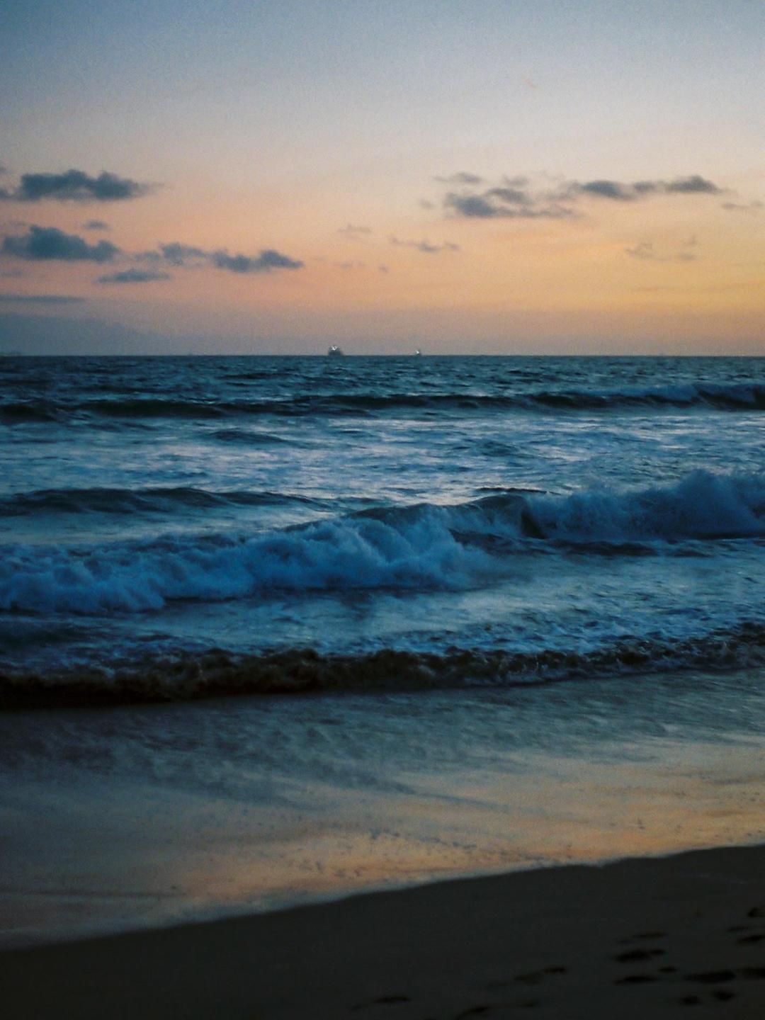 Waves crash on a beach under a colorful sky at dusk.