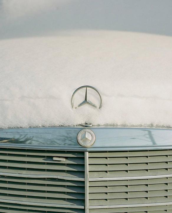 A close-up shot shows the front of a car covered in snow, with the Mercedes-Benz emblem visible.