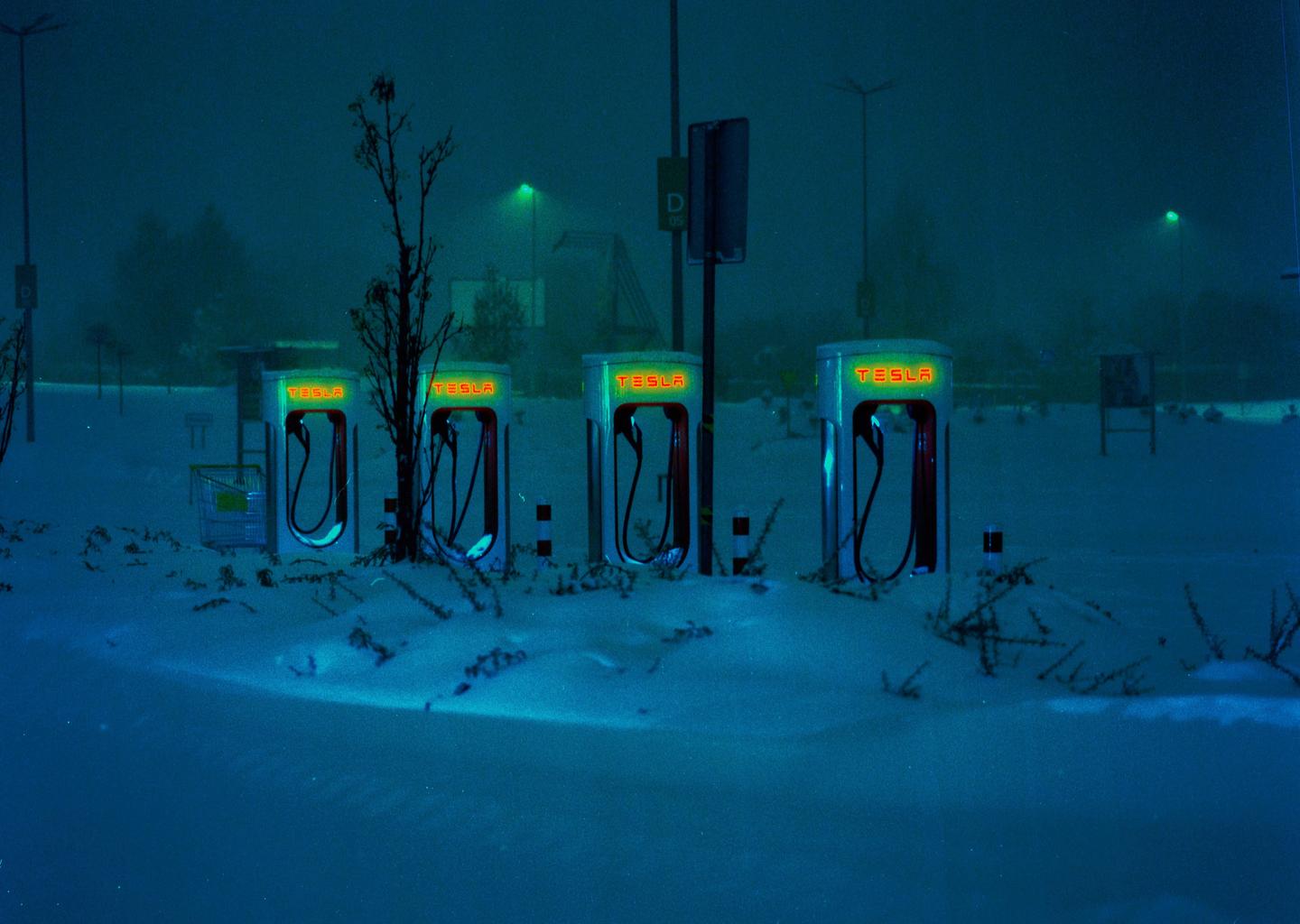Four Tesla charging stations stand in a snow-covered landscape at night.