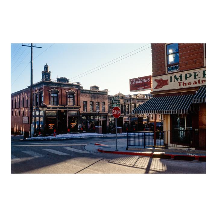A street corner in a historic town features brick buildings, a stop sign, and a crosswalk with long shadows.