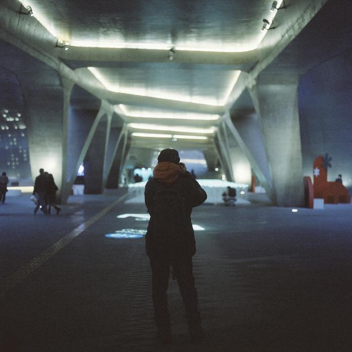 A person stands with their back to the camera, looking down a brightly lit, modern, concrete tunnel at night.