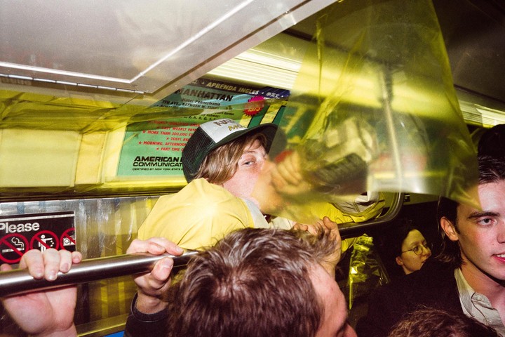 A man in a yellow shirt and a cap is kissing a woman behind a yellow plastic sheet on a crowded subway.