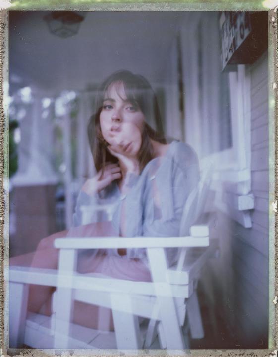 A woman with long hair sits on a white chair with a double exposure effect.