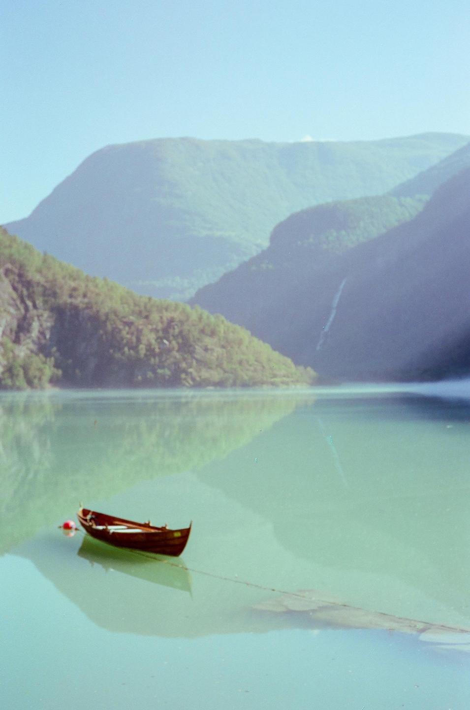 A small wooden boat floats on a calm body of water with mountains in the background.