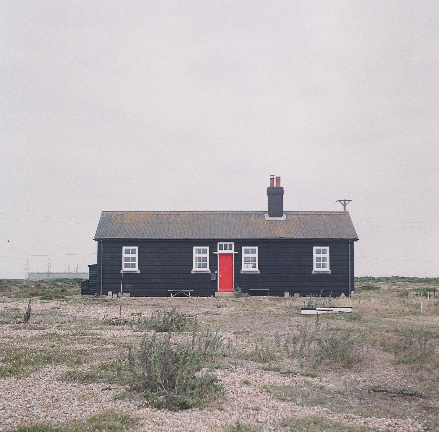 A black house with a red door stands in a desolate, rocky landscape under an overcast sky.