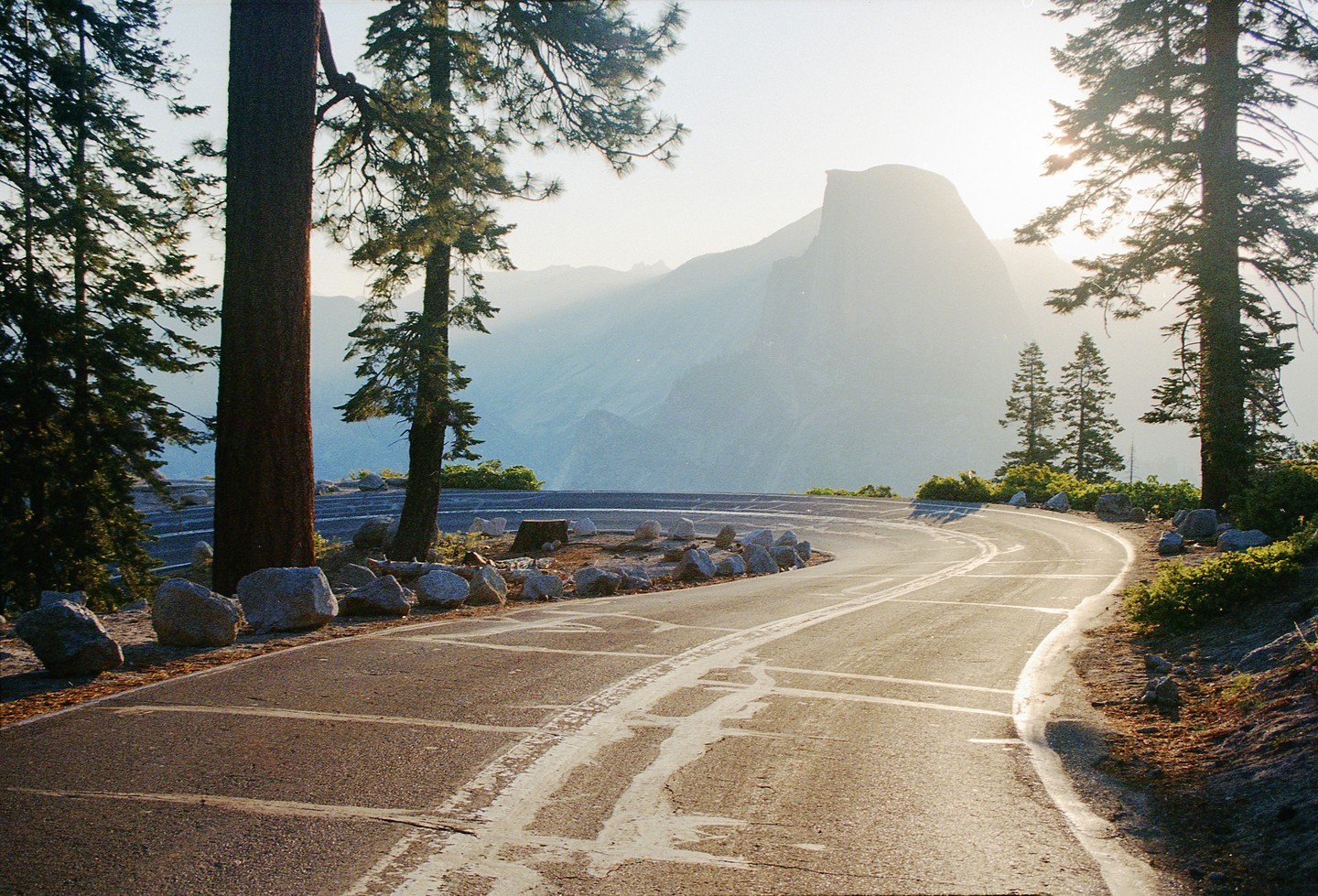 A winding road curves through a forest with a large mountain in the hazy background.