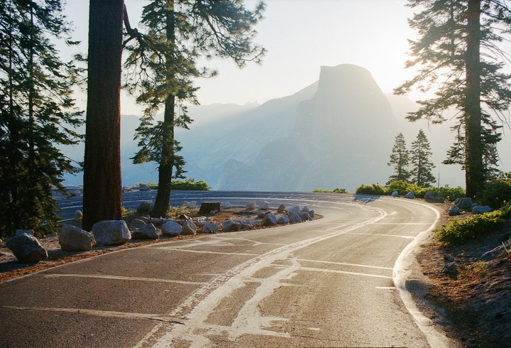 A winding road curves through a forest with a large mountain in the hazy background.