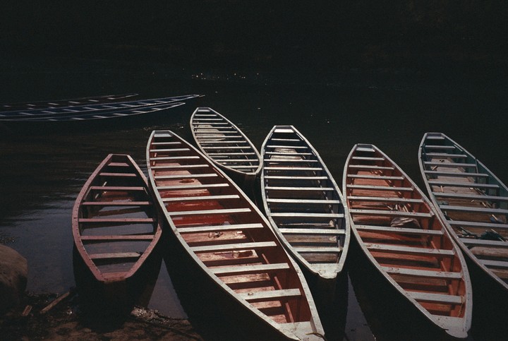 Several wooden boats are docked along a dark riverbank, with more boats visible in the distance.
