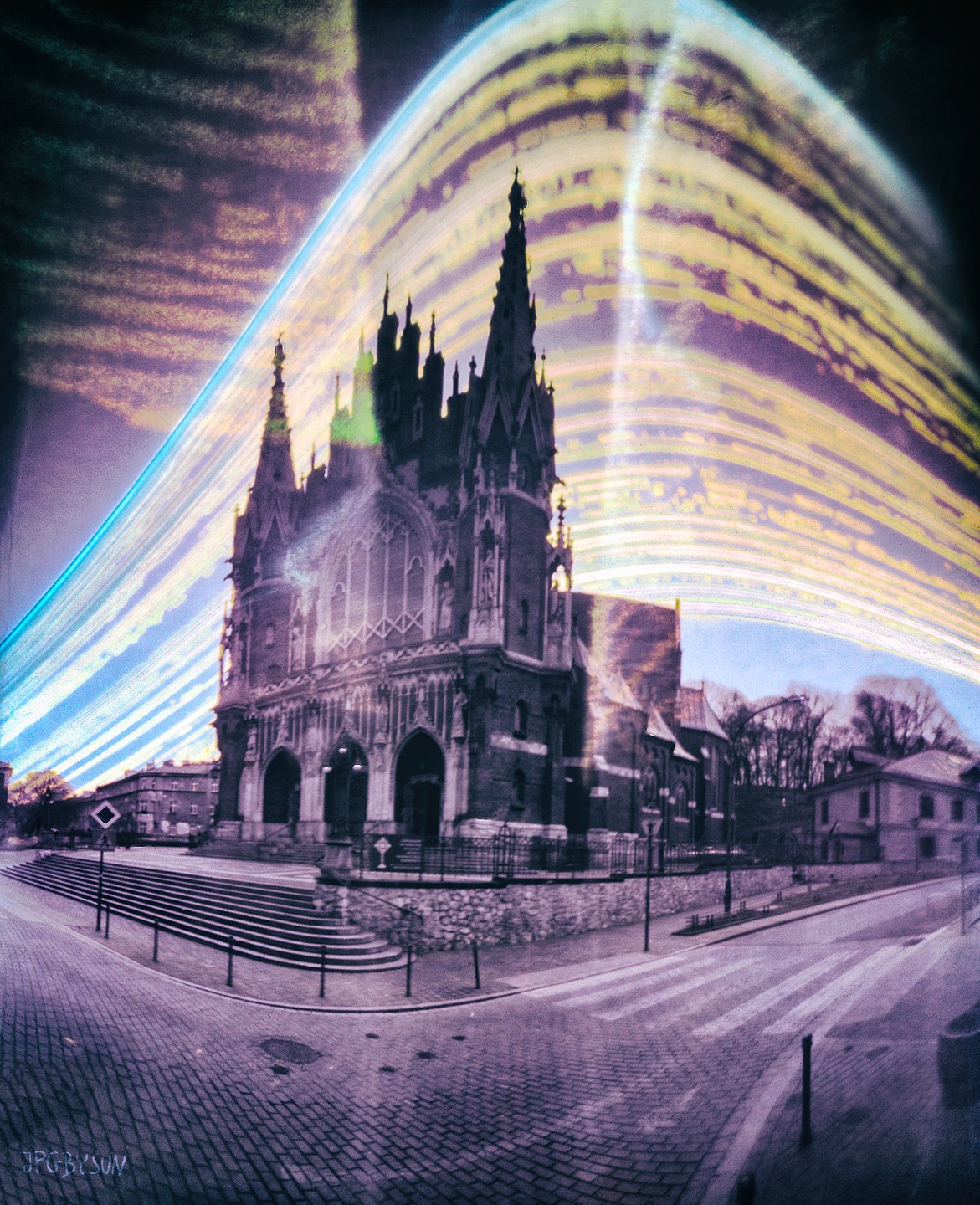 A church with tall spires stands on a street corner with light trails streaking across the sky.