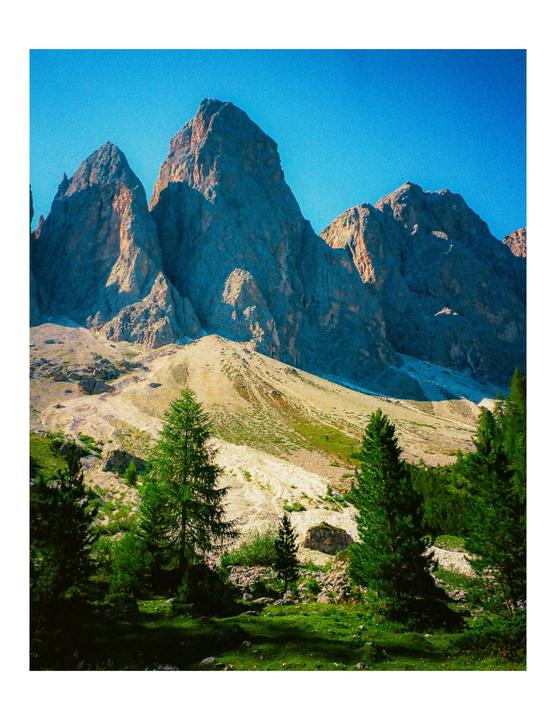 A mountain range with trees and a grassy slope is visible under a clear blue sky.