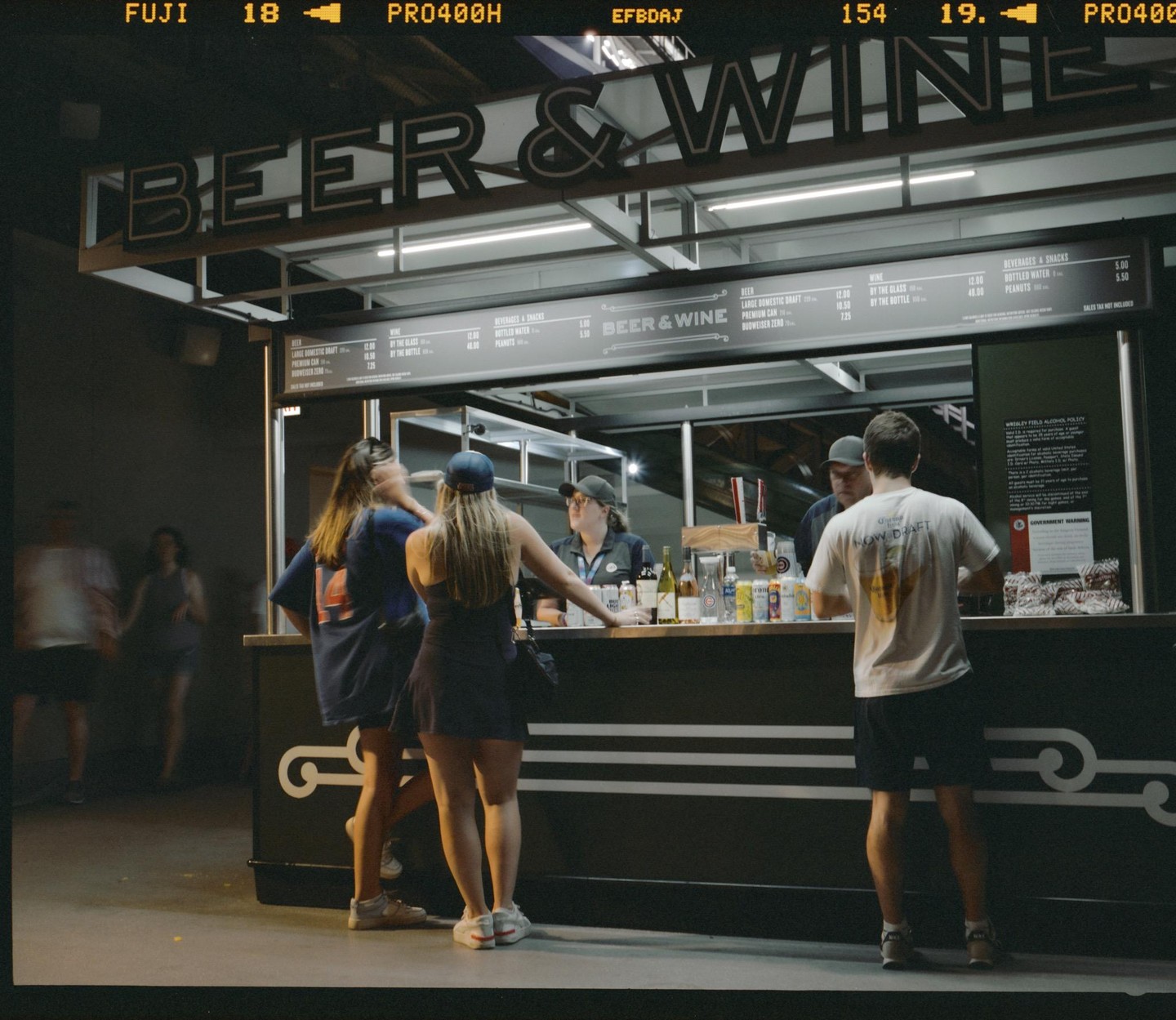 A group of people stand at a beer and wine concession stand at night.