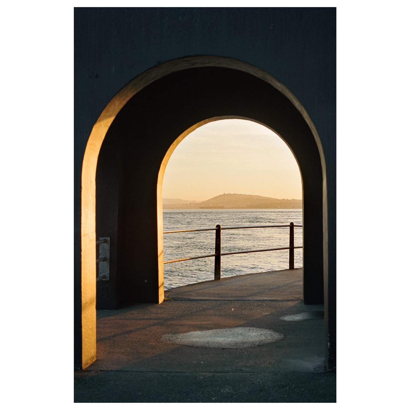 A view through an archway shows a body of water with a distant hill under a golden sky.