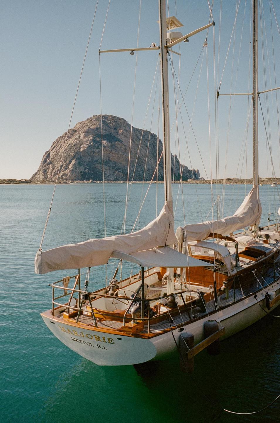 A sailboat is docked in a harbor with a large rock formation in the background.