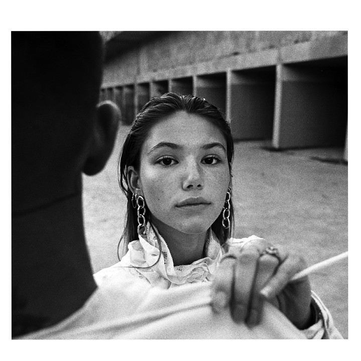 A woman with long earrings looks at the camera over the shoulder of a man.