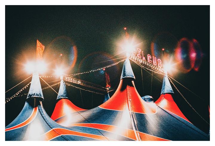 A red and blue circus tent with bright lights and a "CIRCUS" sign is visible at night.