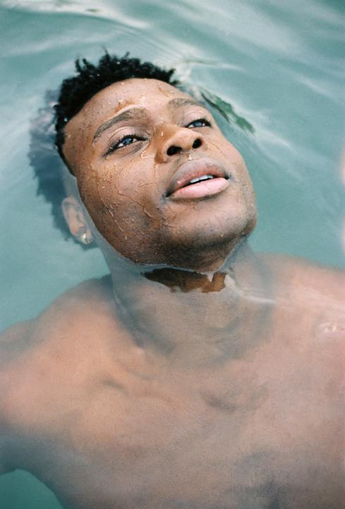 A man with water droplets on his face is looking up while submerged in water.