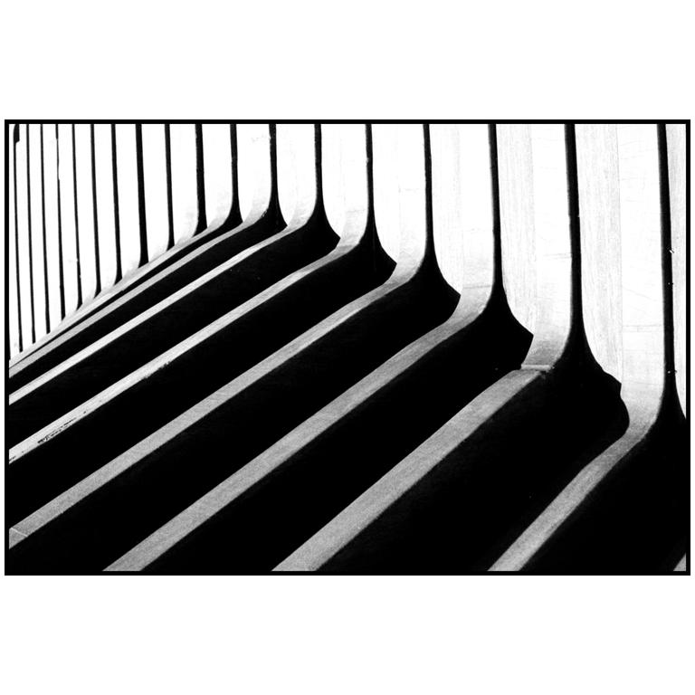 A series of vertical architectural elements cast long, diagonal shadows across a surface.