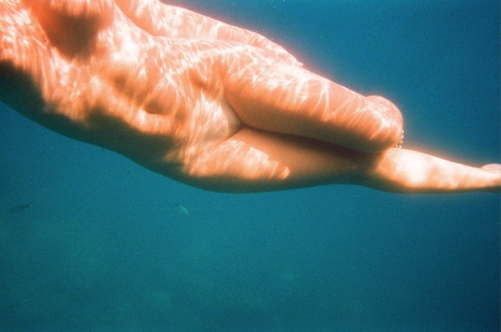 A person's body is visible underwater with light patterns on the skin.