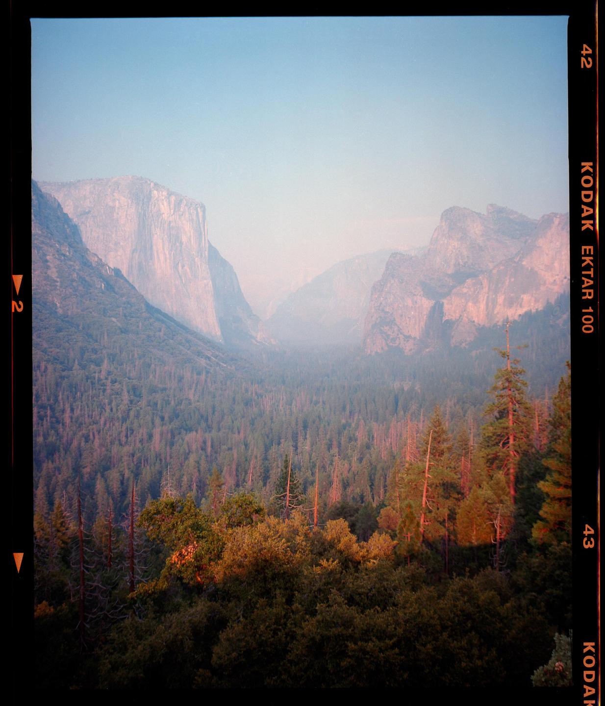 A hazy valley with mountains and a forest is visible under a clear sky.