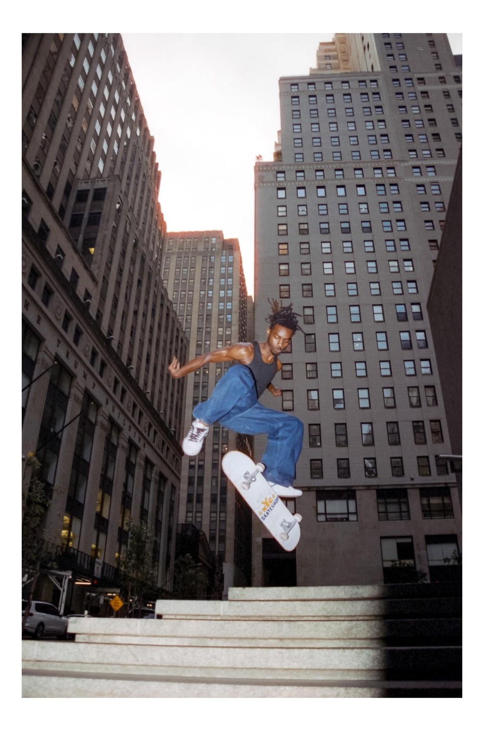 A man on a skateboard jumps in the air in front of tall buildings.