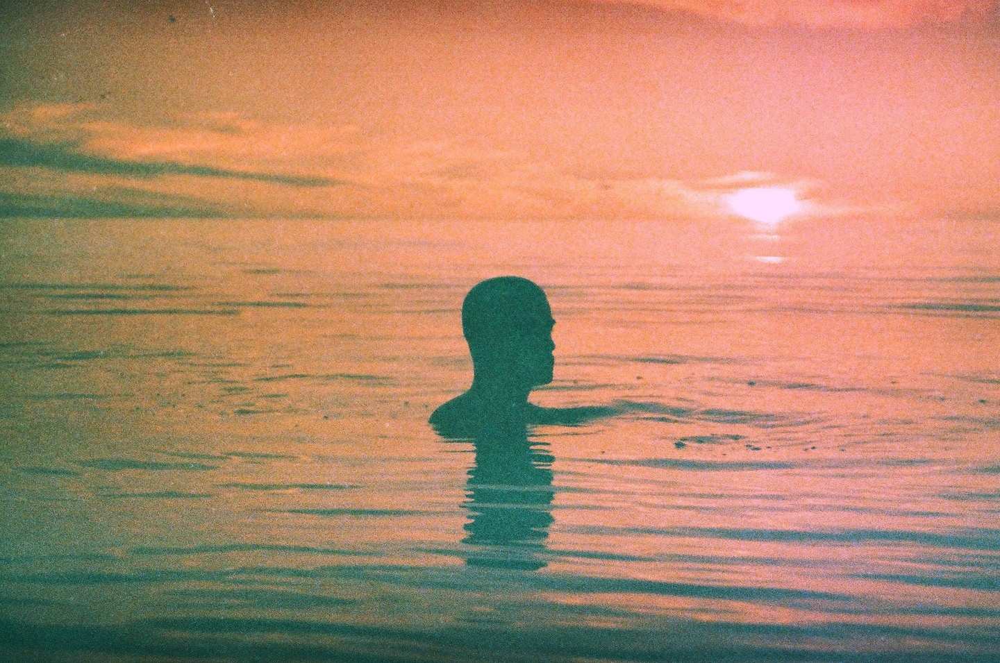 A person's silhouette is visible in the water at sunset.