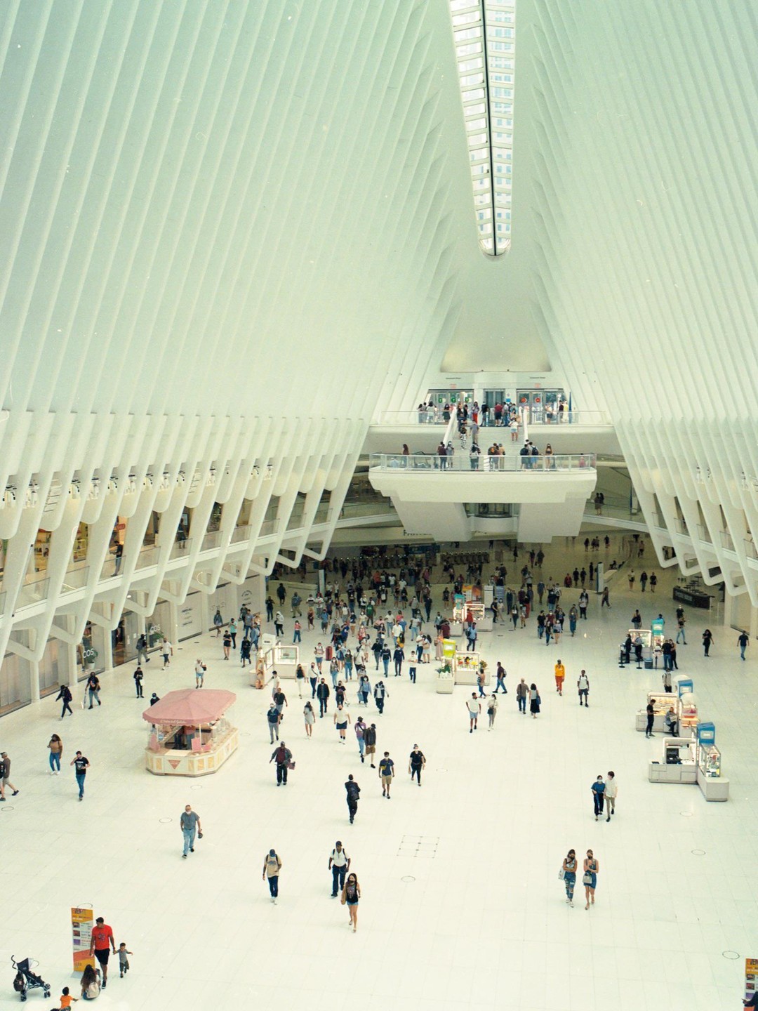 A large crowd of people walk through a bright, modern, white building with a high, vaulted ceiling.