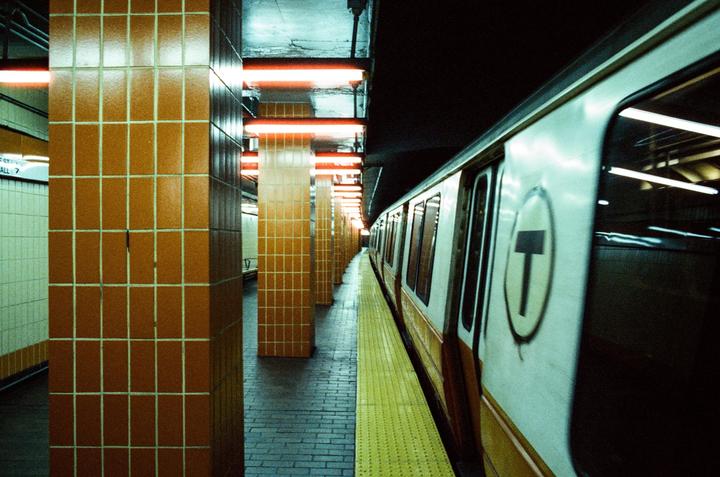 A subway train is stopped at a station platform with orange tiled pillars and neon lights.