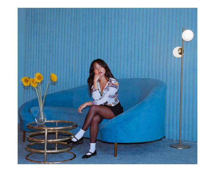 A woman sits on a blue sofa next to a coffee table with sunflowers and a floor lamp.