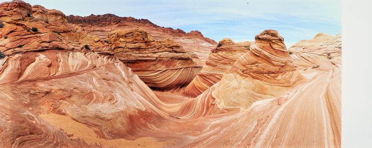 A panoramic view shows a desert landscape with swirling rock formations under a blue sky.