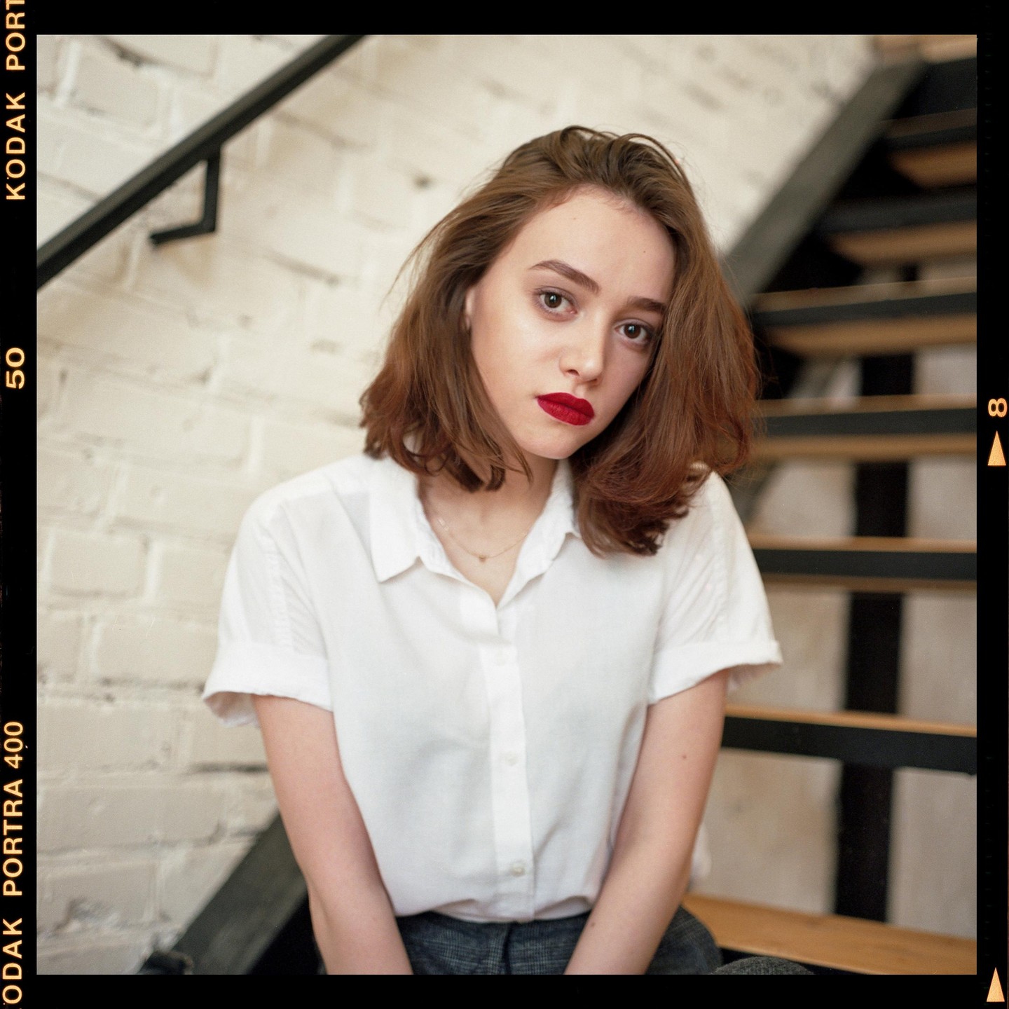 A woman with red lipstick and a white shirt is sitting on a staircase.