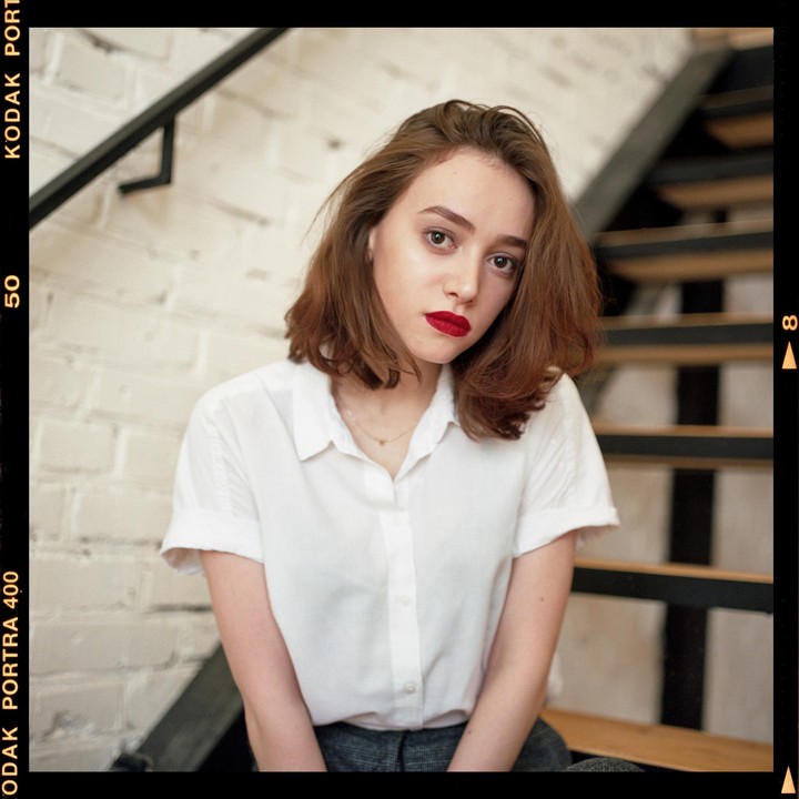A woman with red lipstick and a white shirt is sitting on a staircase.