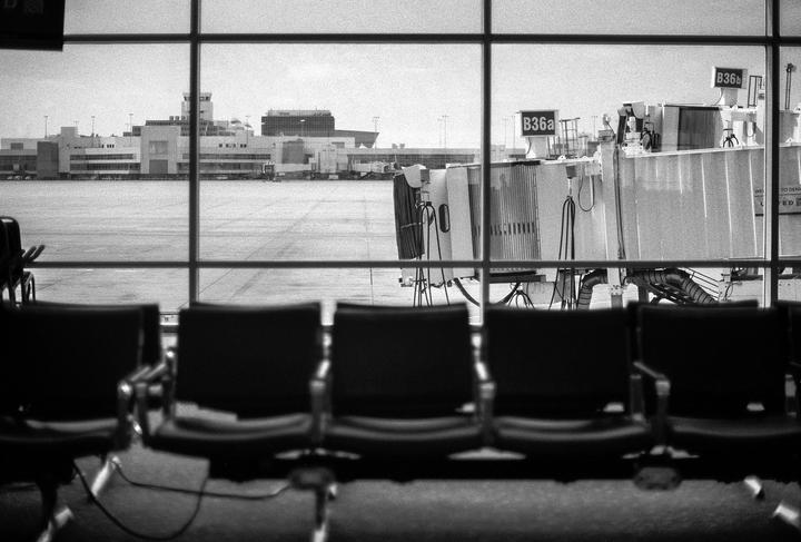 A row of empty chairs faces a large window overlooking an airport terminal and jet bridge.