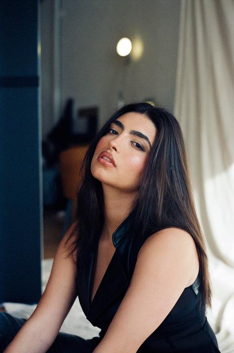 A woman with long dark hair and a black top looks directly at the viewer.