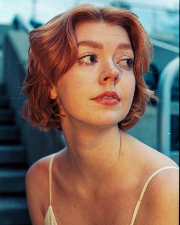 A woman with short red hair looks to the side, illuminated by warm light.