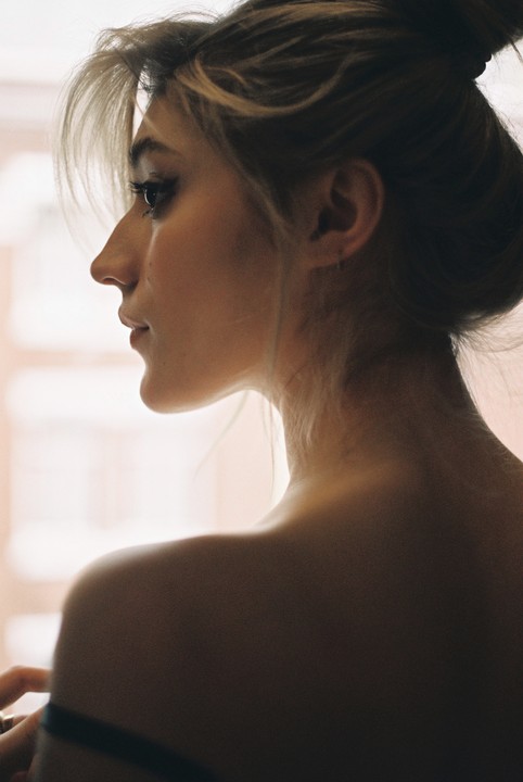 A woman with her hair in a bun looks to the left, her back and shoulder visible.