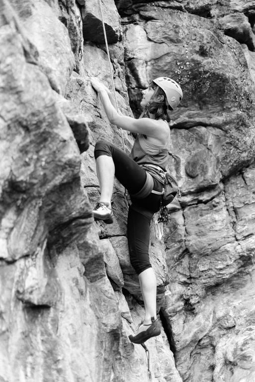 A woman wearing a helmet and harness is rock climbing on a rocky cliff face.