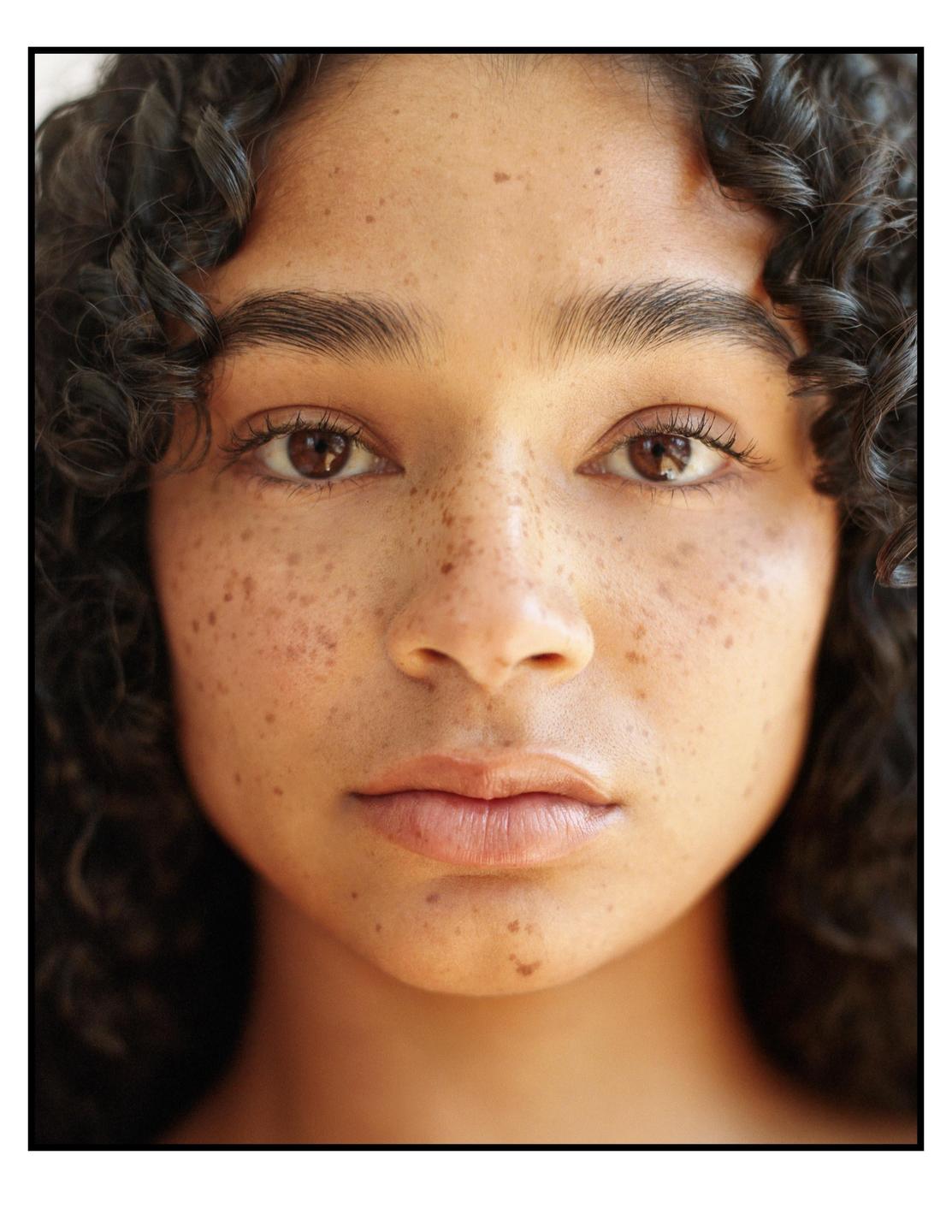 A woman with curly hair and freckles looks directly at the viewer.