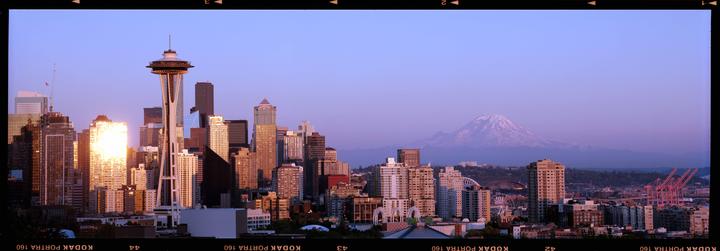 The Seattle skyline is illuminated by the setting sun, with Mount Rainier visible in the distance.