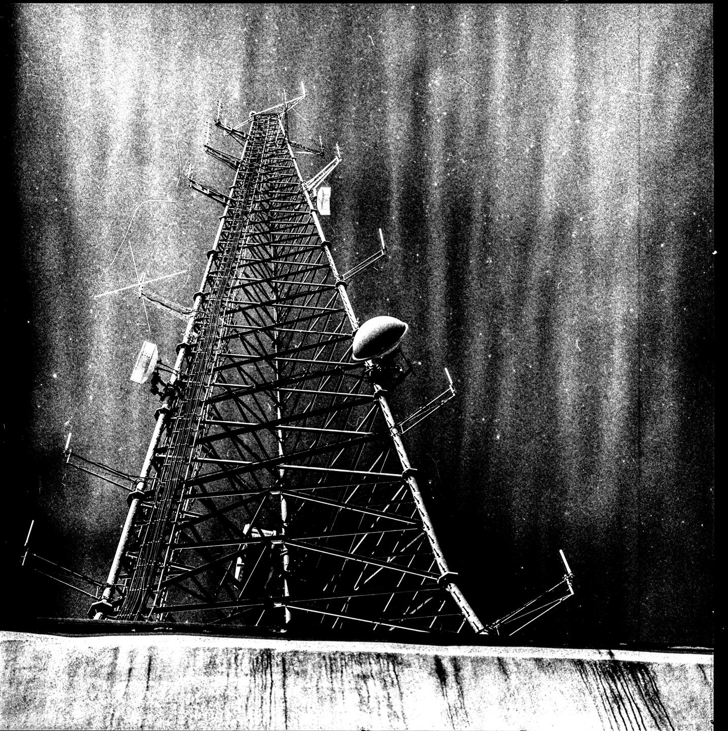 A tall metal tower with various antennas and dishes stands against a dark, textured sky.