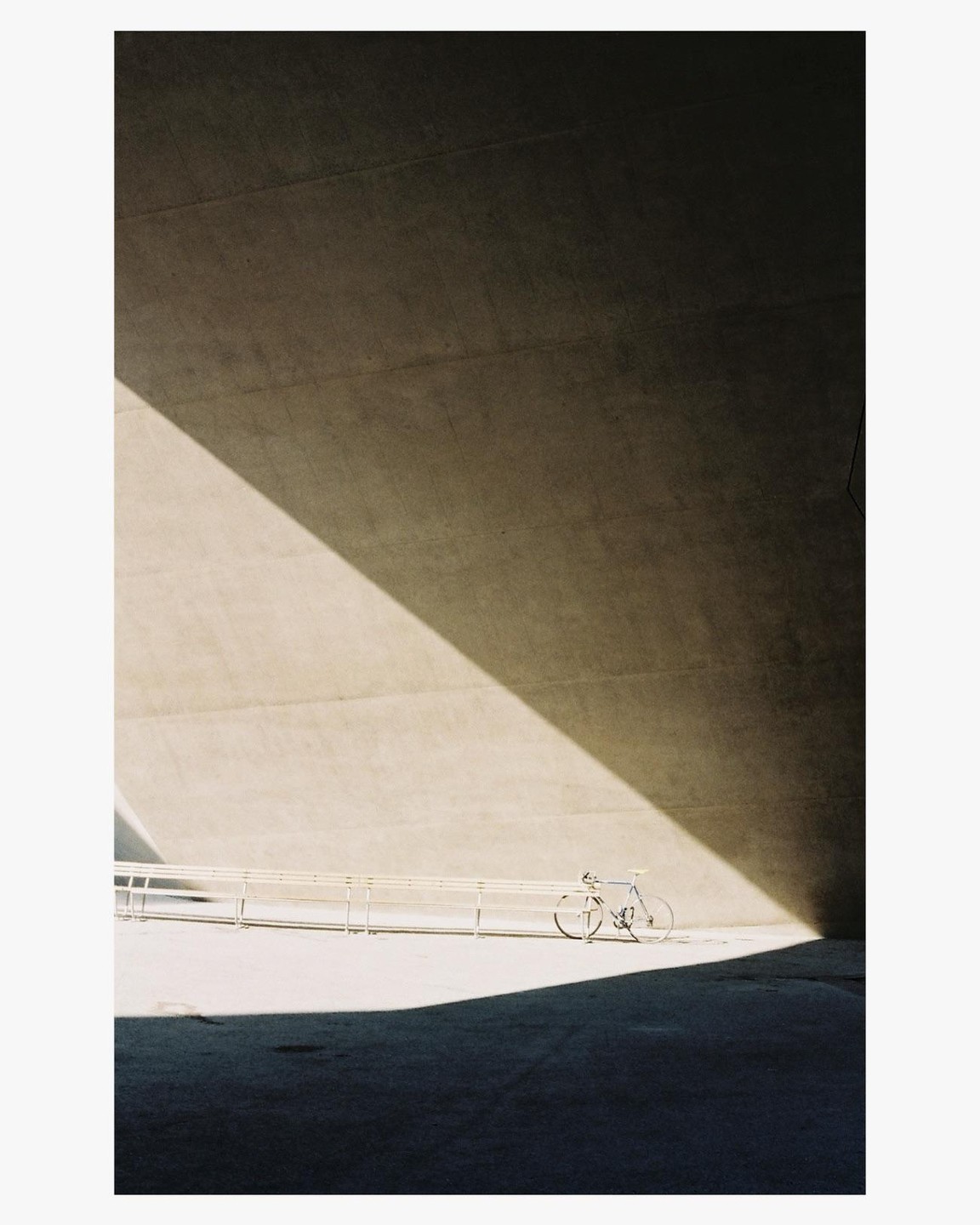 A bicycle is parked against a concrete wall with a strong diagonal shadow.