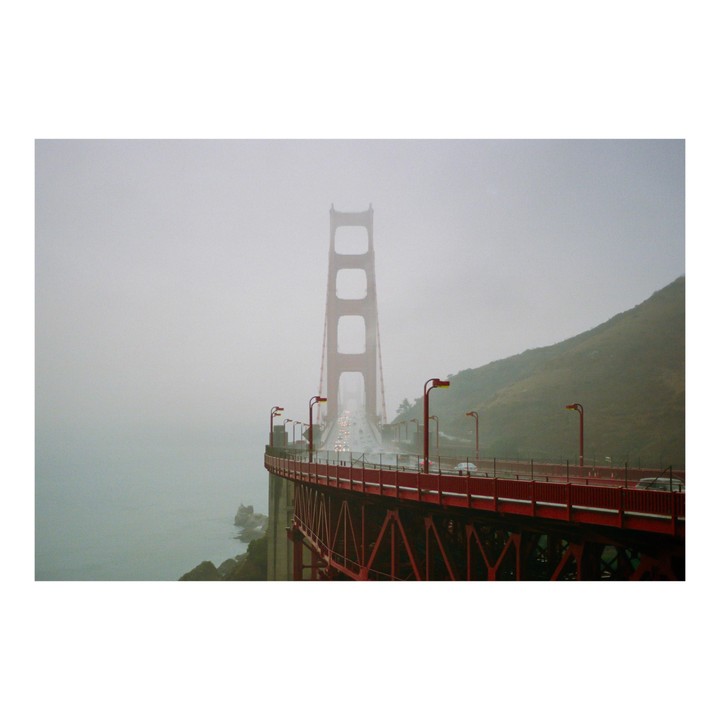 The Golden Gate Bridge is visible through a thick fog, with cars driving across its span.