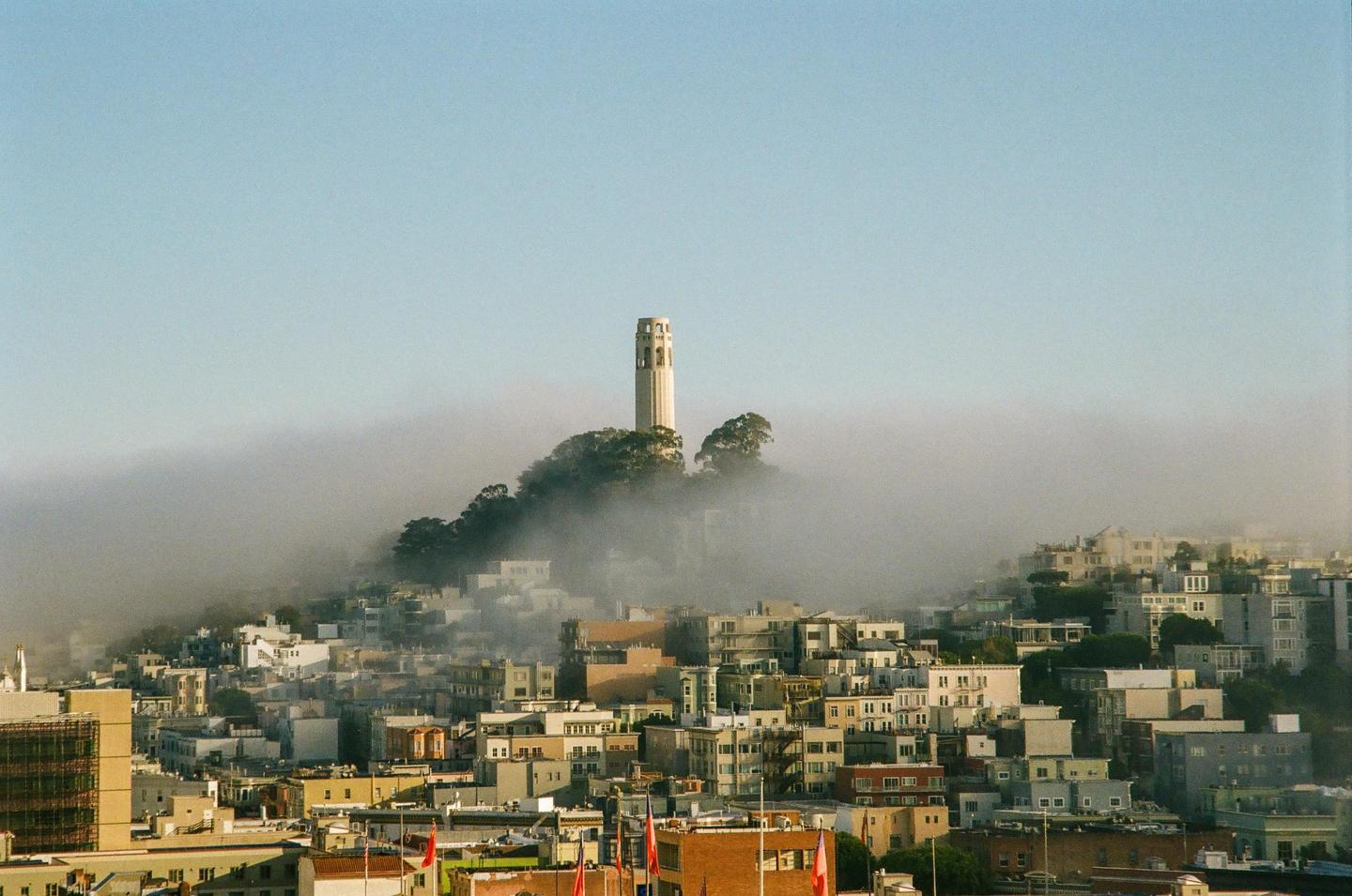 Coit Tower rises above a foggy cityscape in San Francisco.