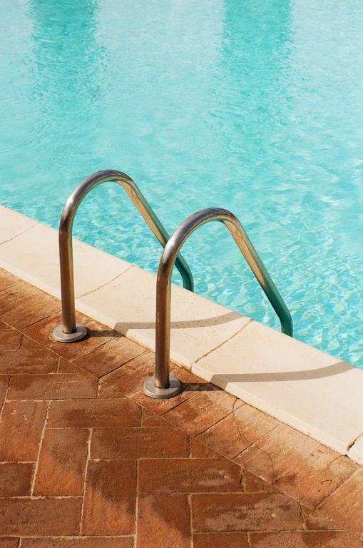 A metal ladder leads into a swimming pool with blue water and a brick deck.