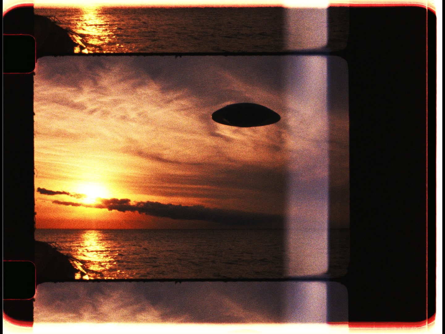 A bright sunset over the ocean is framed by film sprockets and a dark, oval shape in the sky.