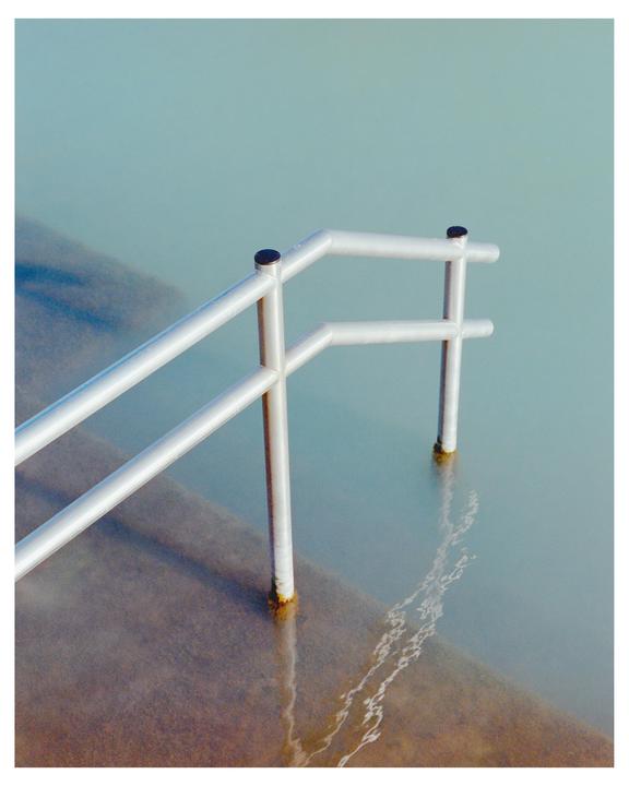 A metal handrail extends into a sea pool with light blue water.