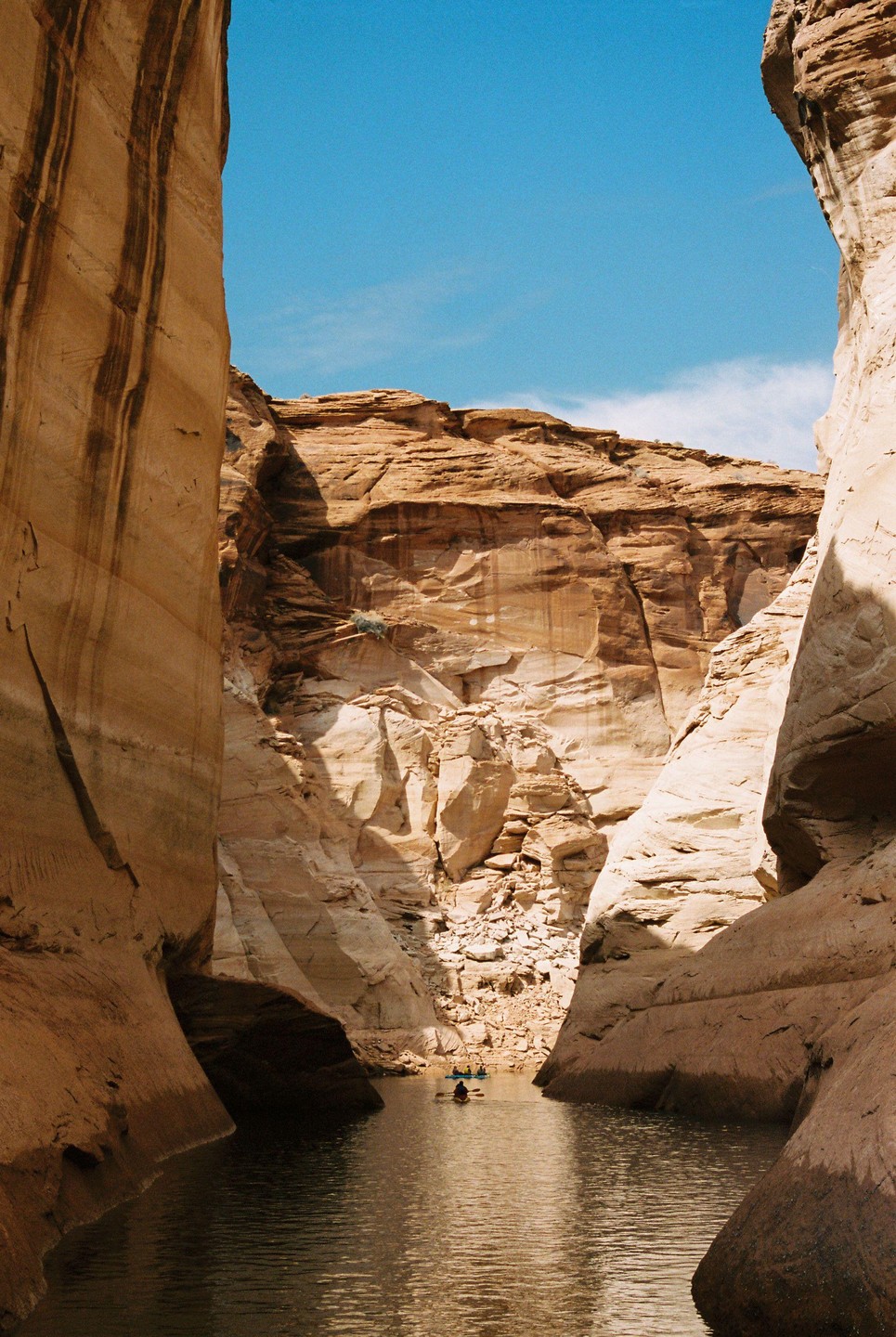 A narrow canyon with towering rock walls on either side opens up to a body of water with kayakers.