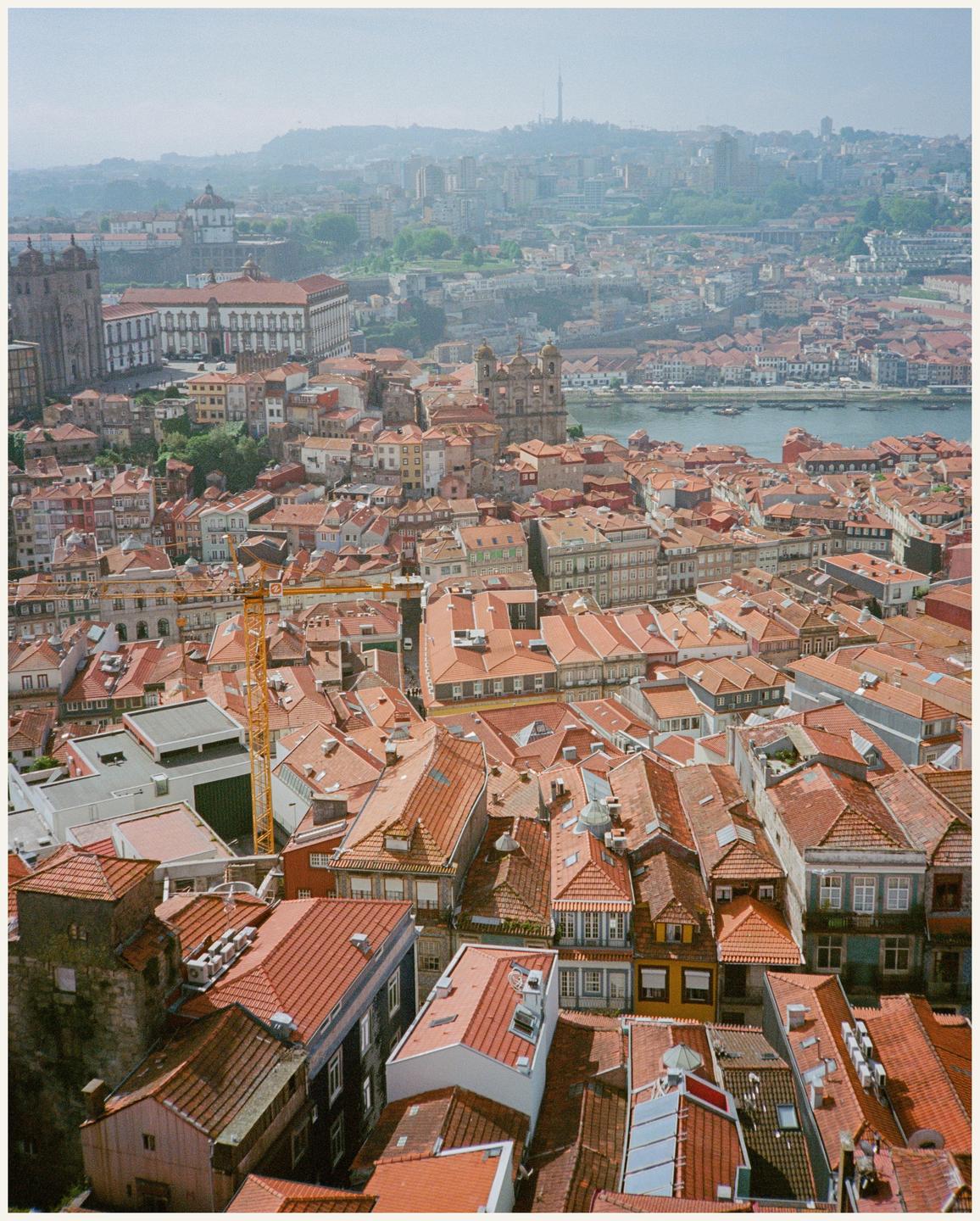A hazy aerial view shows a dense city with red-tiled roofs and a river.