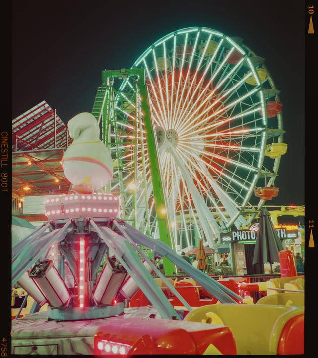 A brightly lit Ferris wheel and another carnival ride glow against the night sky.