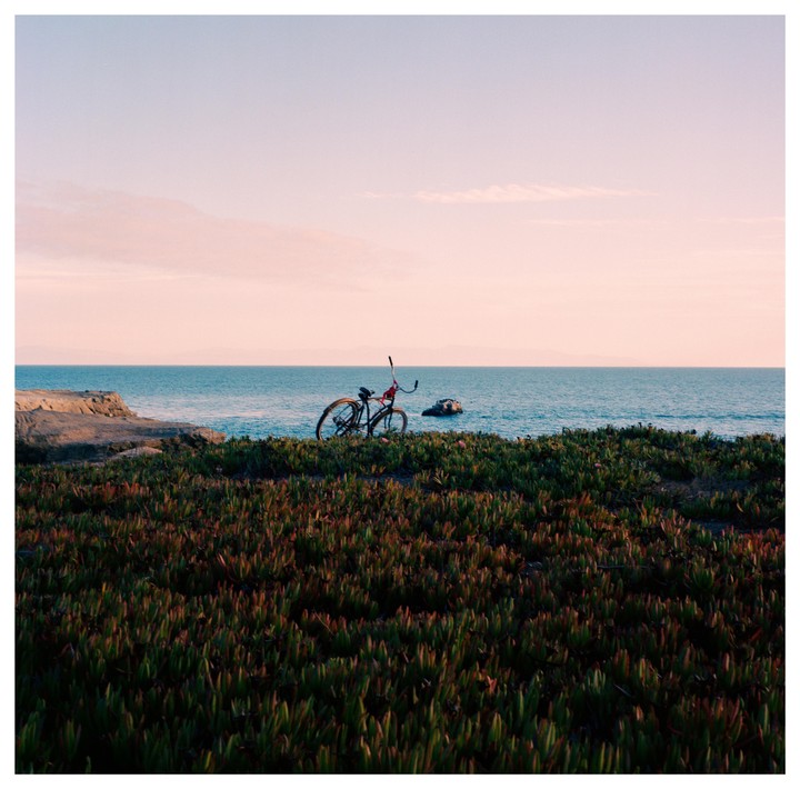 A bicycle is parked on a grassy cliff overlooking the ocean at sunset.