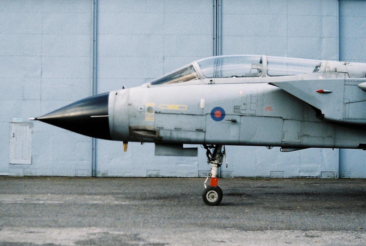 A military jet is parked in front of a light blue hangar.